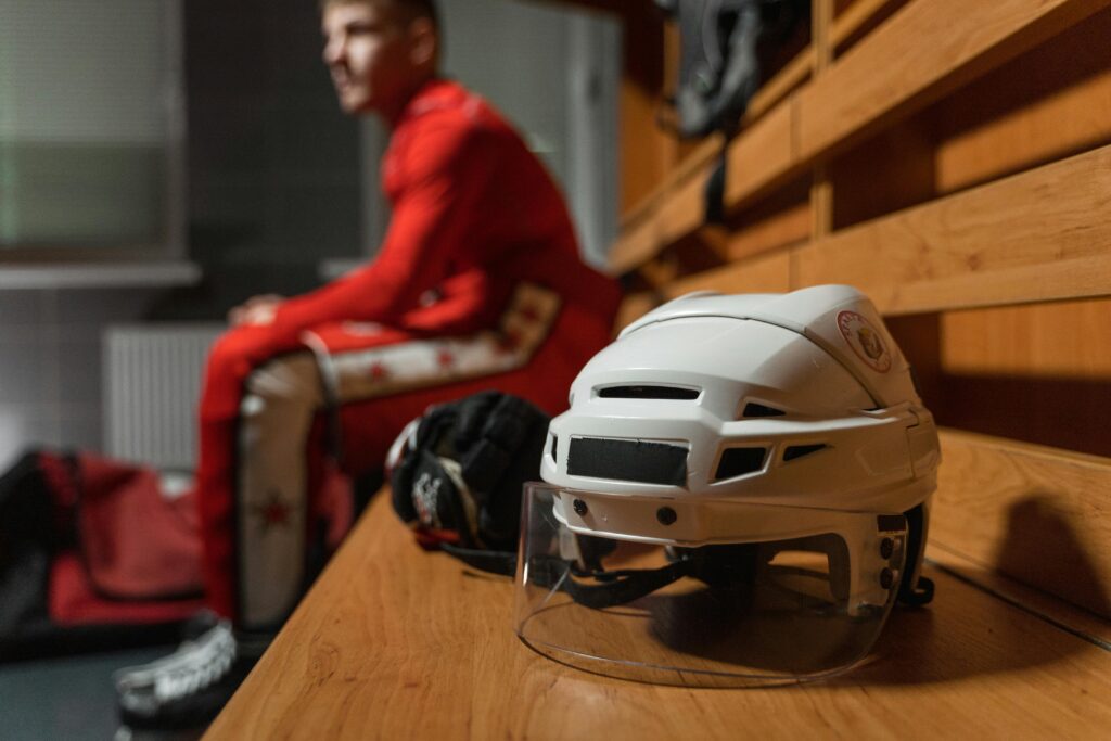 Close-up of hockey helmet and gear on bench with athlete in background.